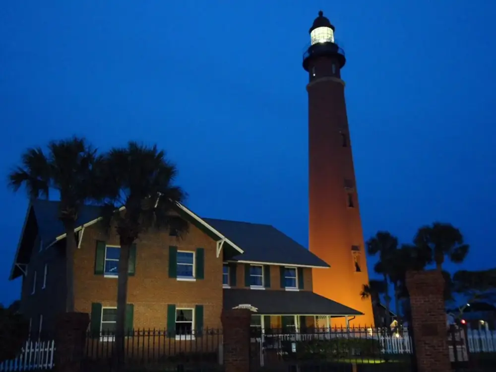 The illuminated Ponce Inlet Lighthouse and keeper buildings at dusk